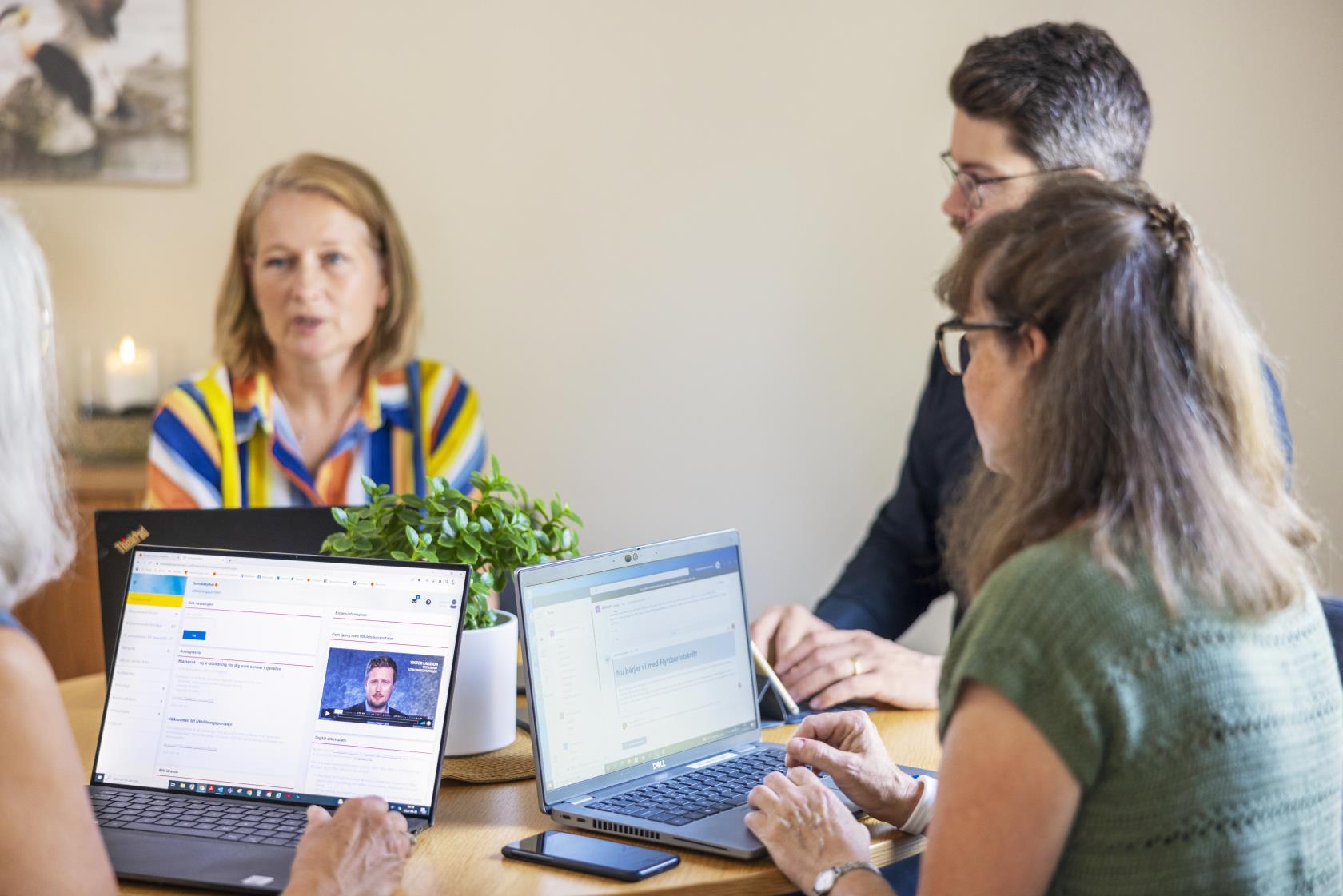 Några personer sitter runt ett bord med varsin laptop och samtalar.