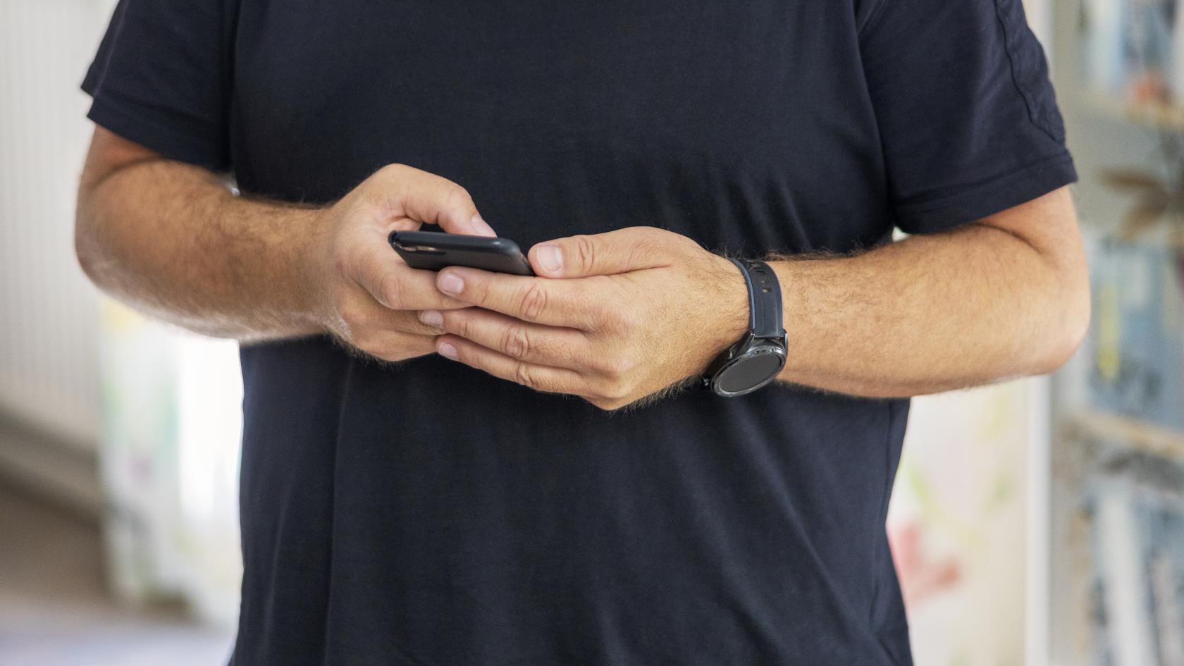 En man från Svenska kyrkan står inomhus med en mobiltelefon i handen.