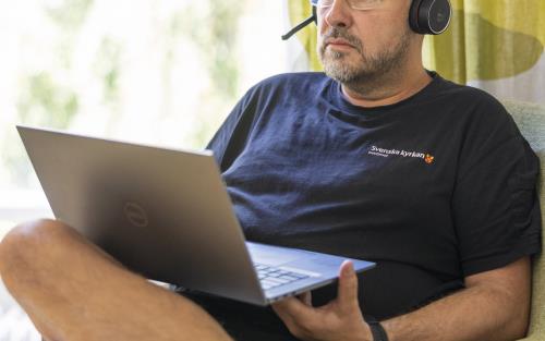 En man med headset sitter i en fåtölj med en laptop i knät.