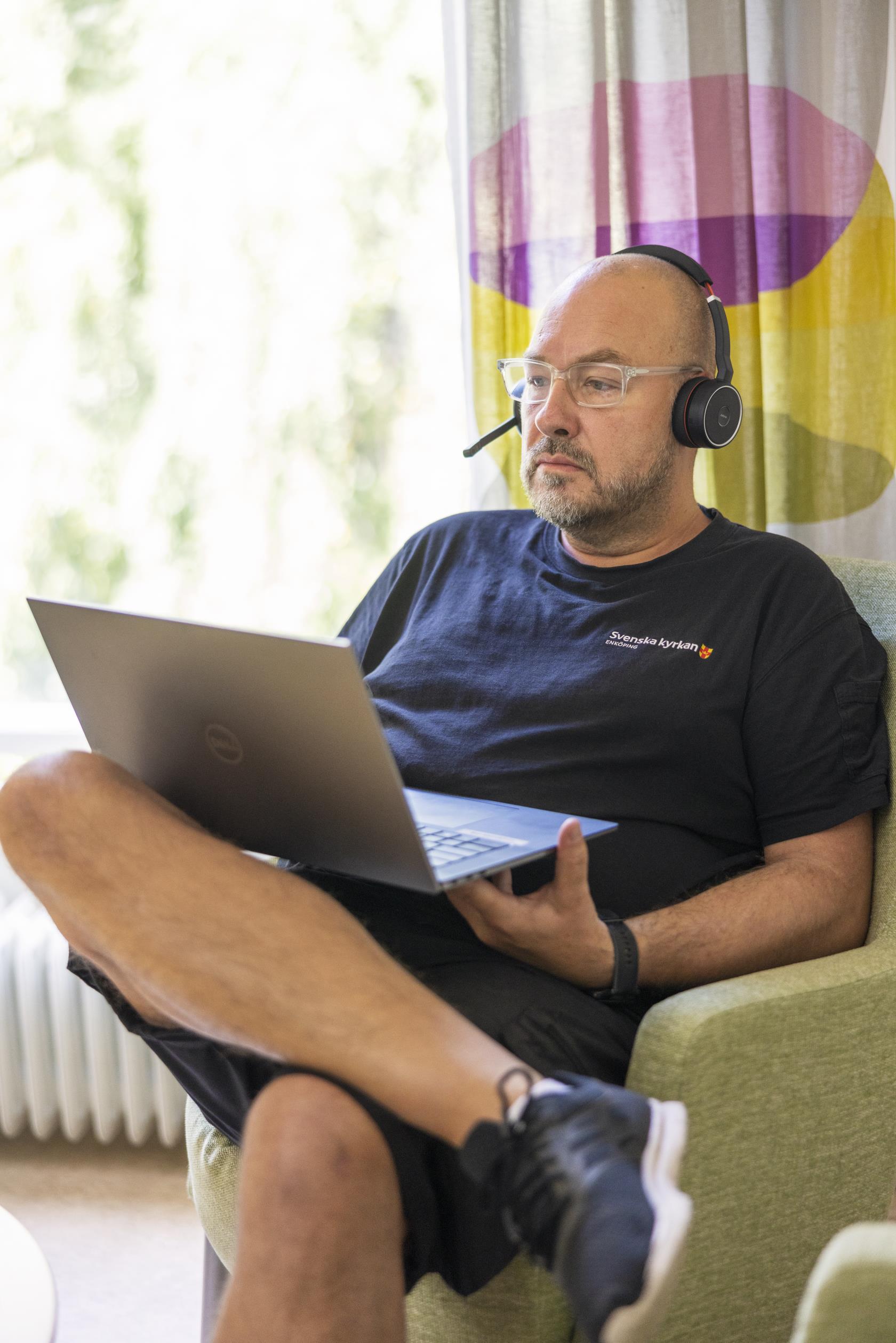 En man med headset sitter i en fåtölj med en laptop i knät.