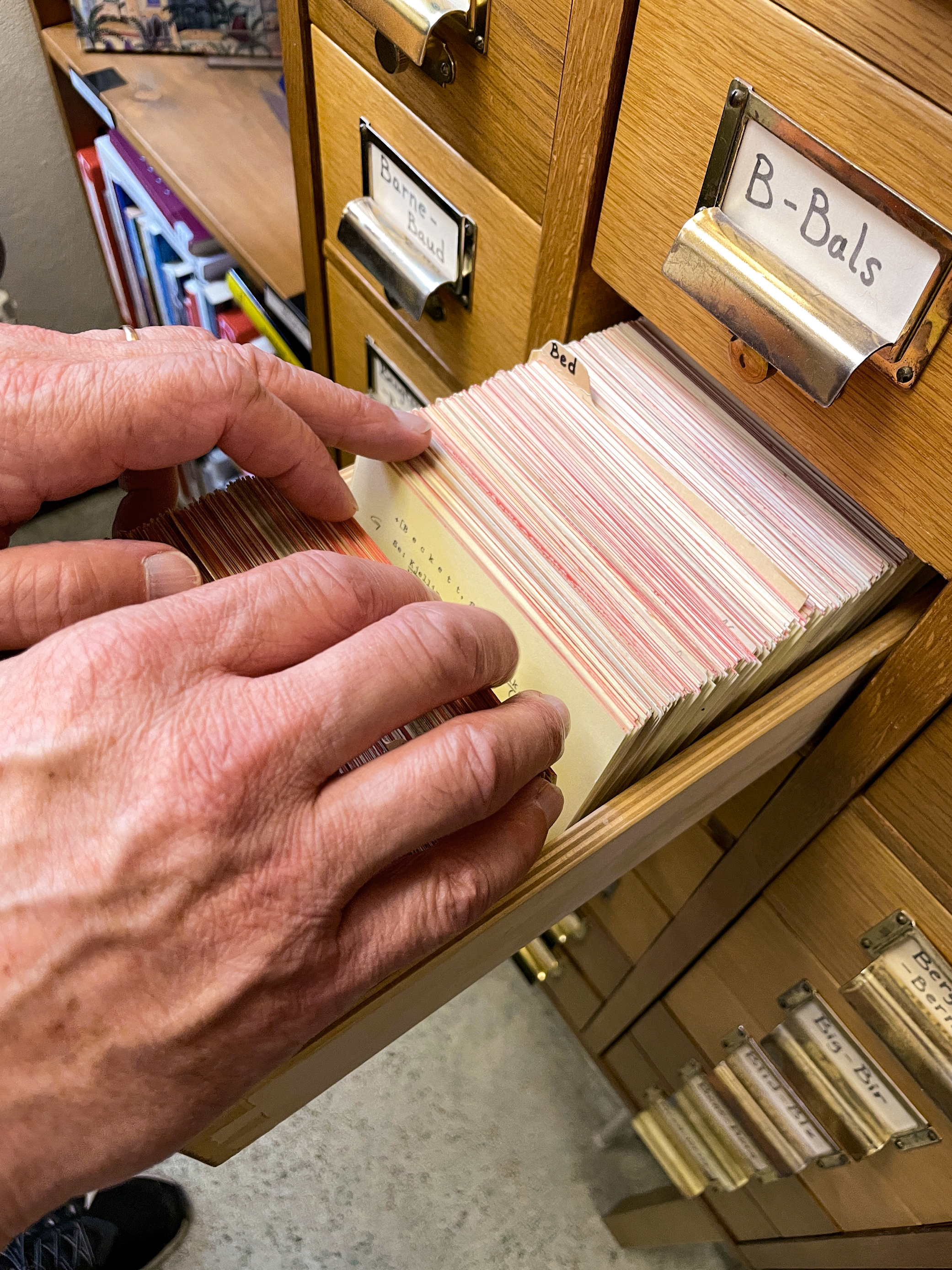 Närbild på två händer som bläddrar i ett kartotek i en gammaldags arkivlåda.