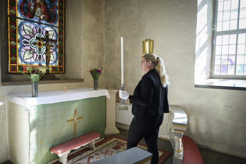 En kvinna med vita handskar ställer två silverljusstakar på ett altare i en kyrka.