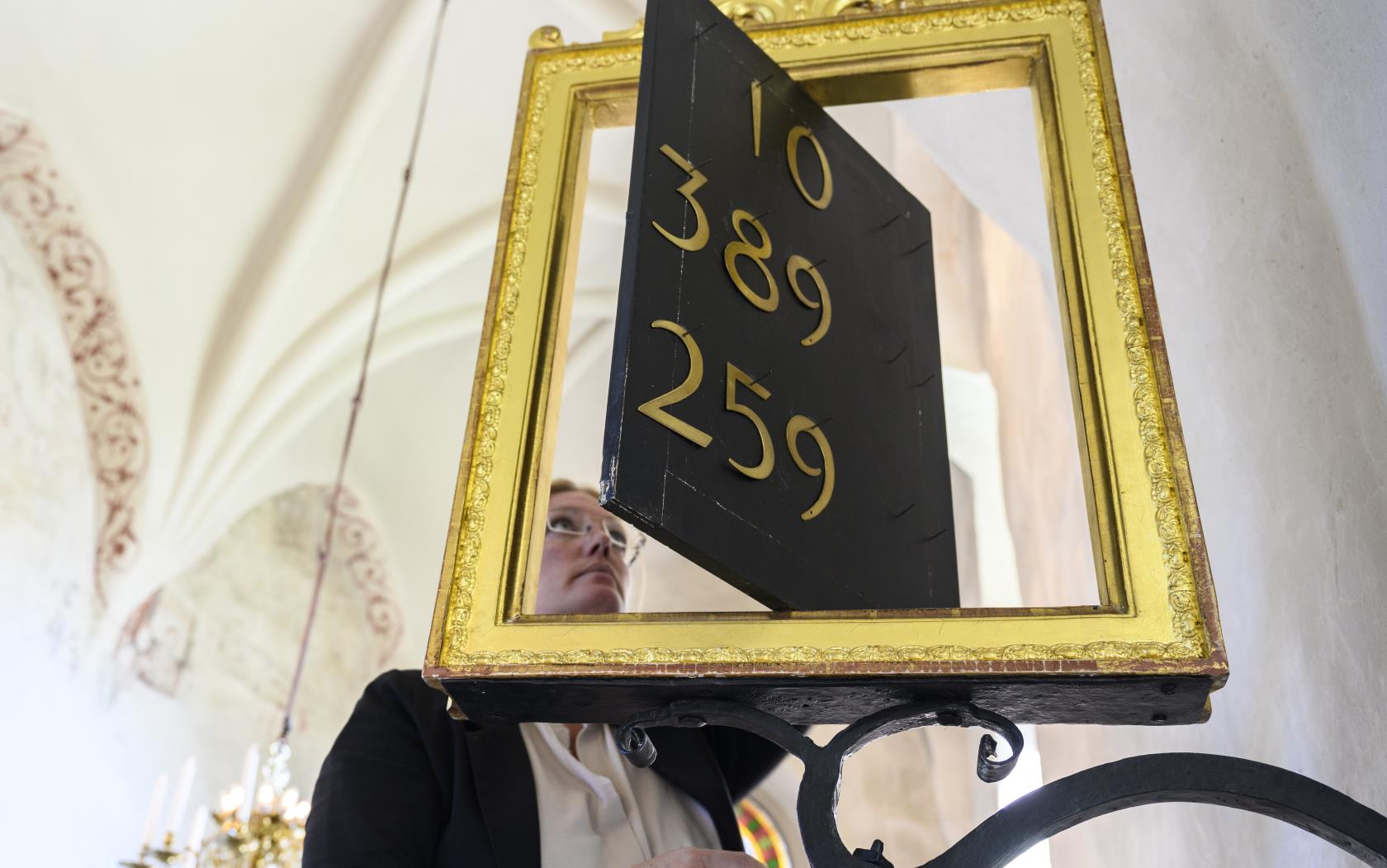 En kvinna justerar siffrorna på en psalmtavla i en kyrka.