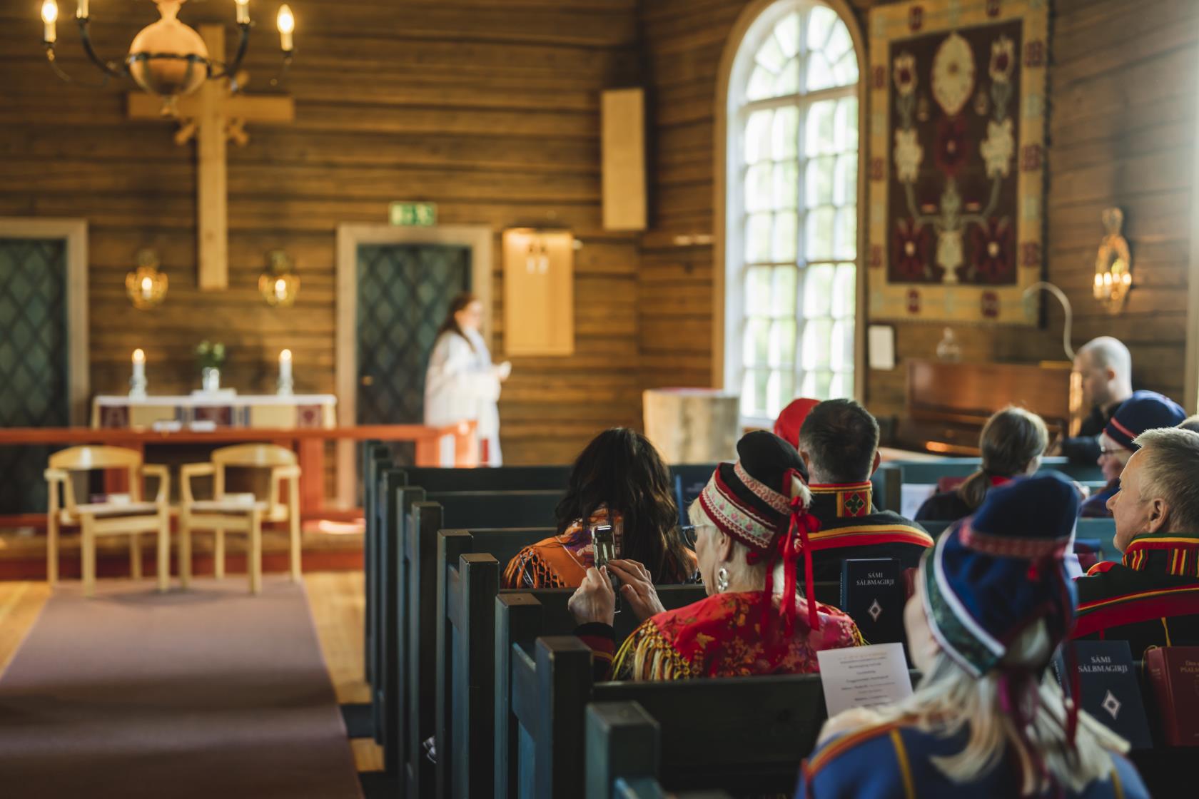 Kyrkobesökare i samiska folkdräkter sitter i kyrkbänkarna.