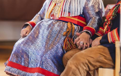 Två personer i samiska folkdräkter sitter och håller varandra i handen.