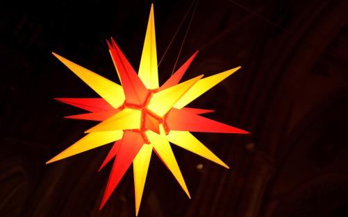 En adventsstjärna hänger från ett kyrktak och lyser i gult och rött.