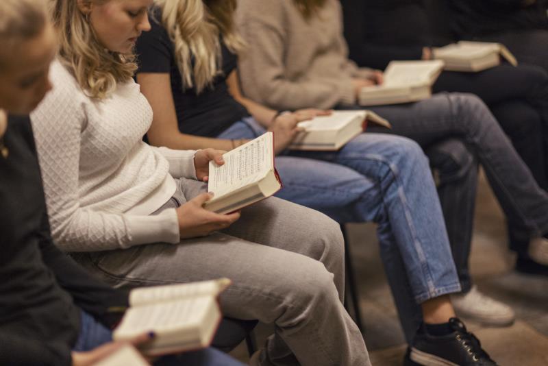 Ungdomar sitter på rad med varsin psalmbok.