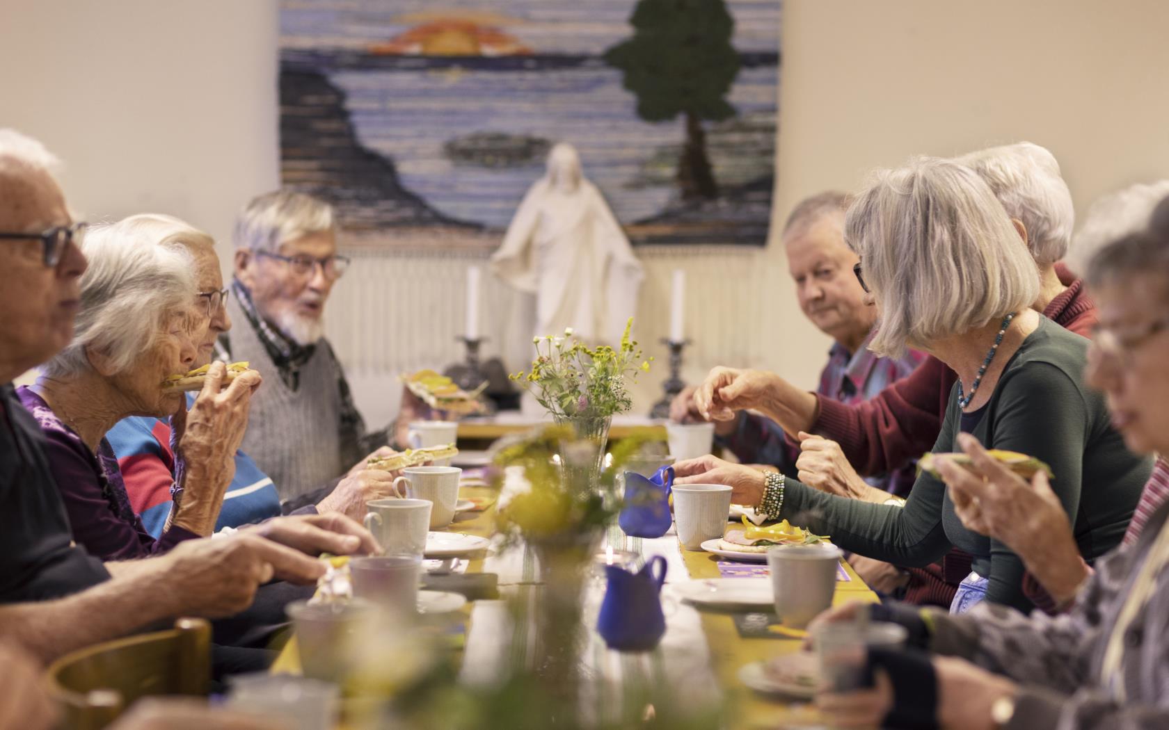 En grupp äldre personer sitter vid ett bord och fikar tillsammans.