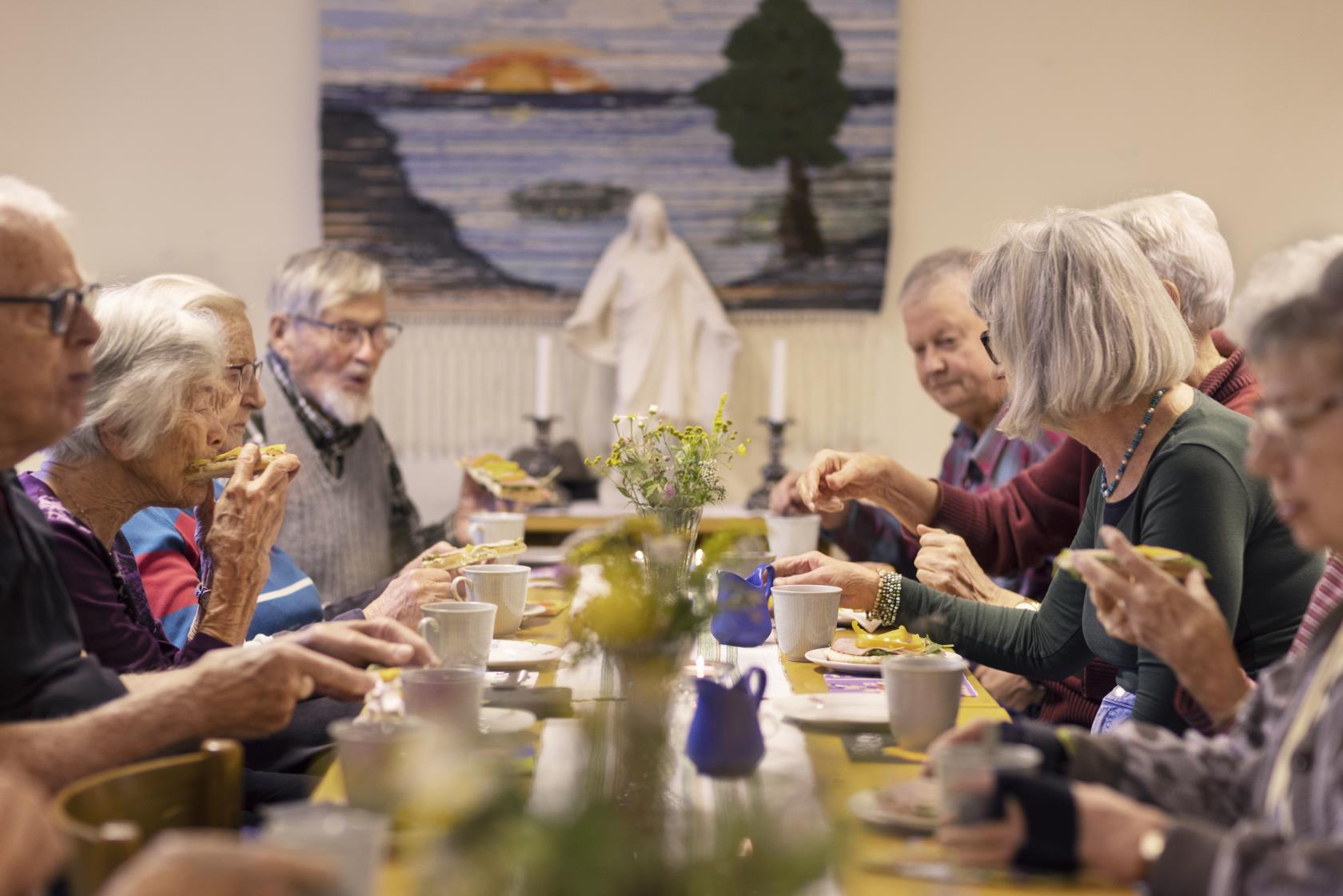 En grupp äldre personer sitter vid ett bord och fikar tillsammans.