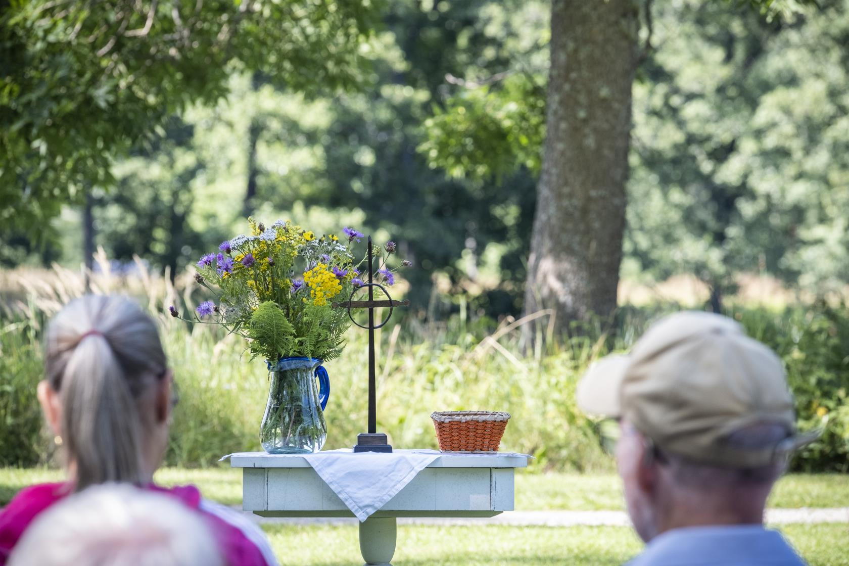 Ett litet träbord har gjort till ett utomhusaltare utsmyckat med ett kors, en liten korg och en blombukett i en vas.