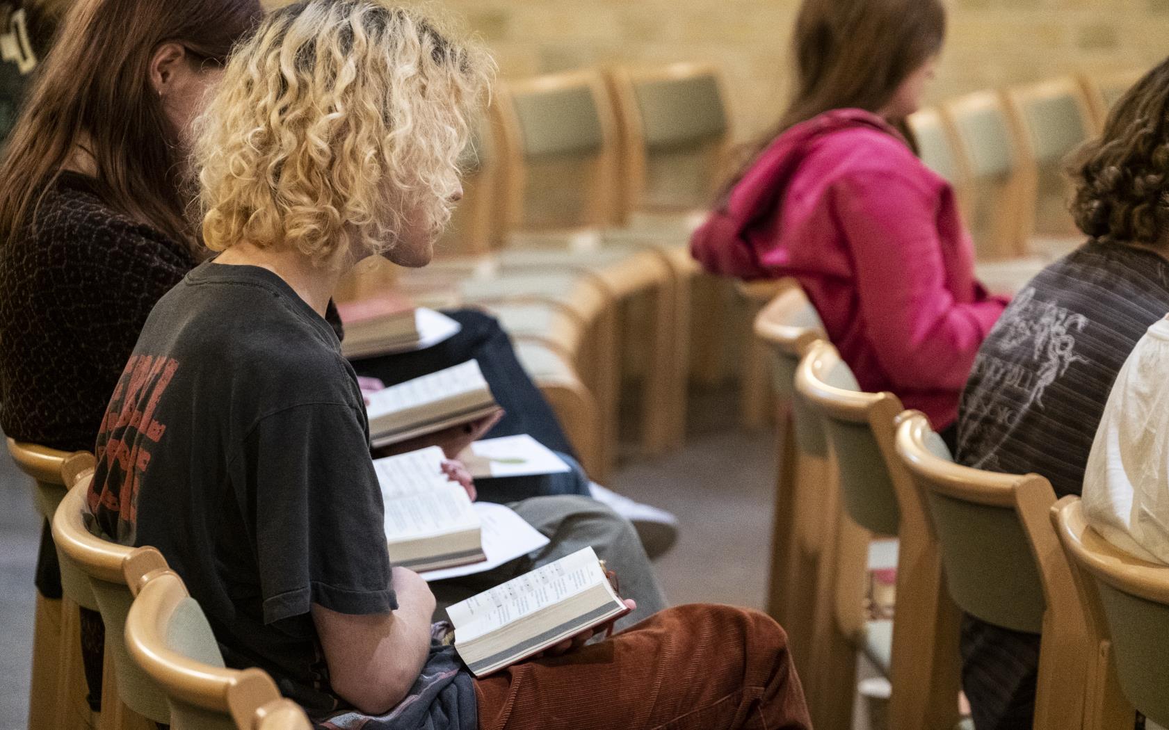 Några ungdomar sitter med psalmböcker i knät i en stolsrad.