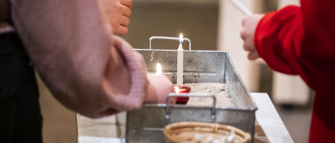 Några personer placerar tända stearinljus i en liten plåtlåda fylld med sand.