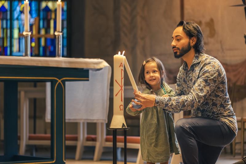 En man och en liten flicka tänder ett dopljus i kyrkan.