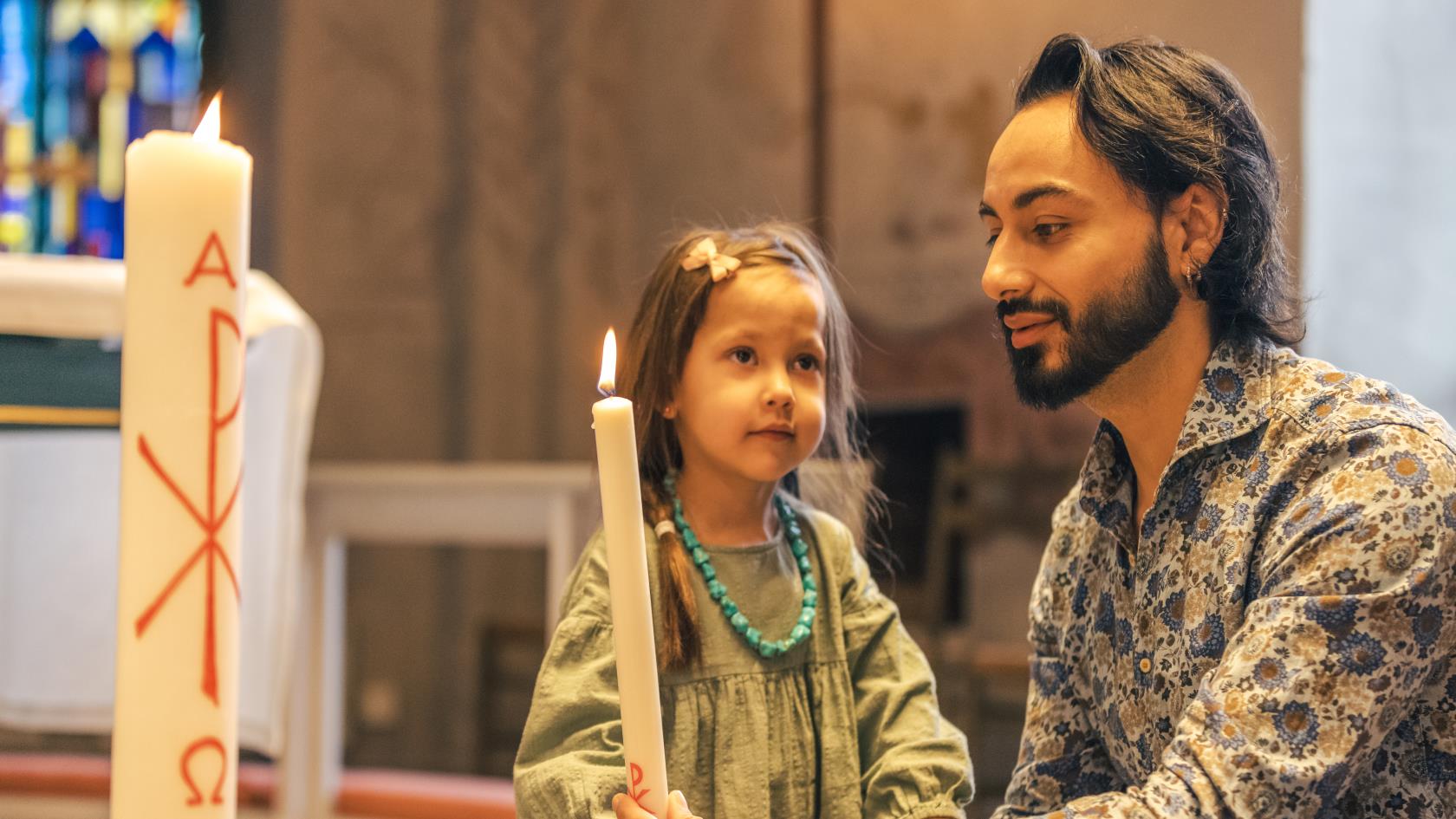 En man och en liten flicka tänder ett dopljus i kyrkan.