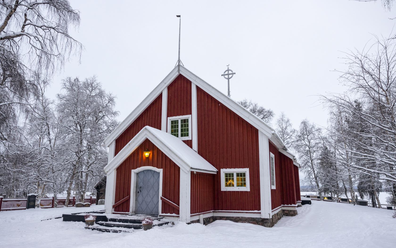 En liten röd träkyrka i ett snöigt landskap.