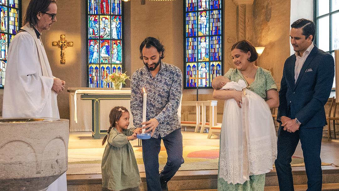 Ett dop i en kyrka. En liten flicka bär ett dopljus för att överlämna till det nydöpta barnet.