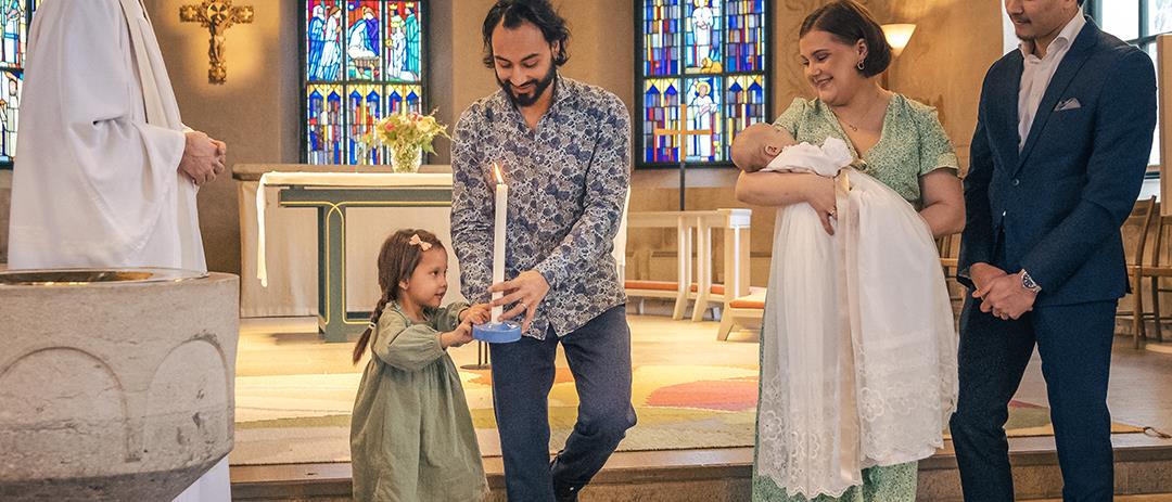 Ett dop i en kyrka. En liten flicka bär ett dopljus för att överlämna till det nydöpta barnet.