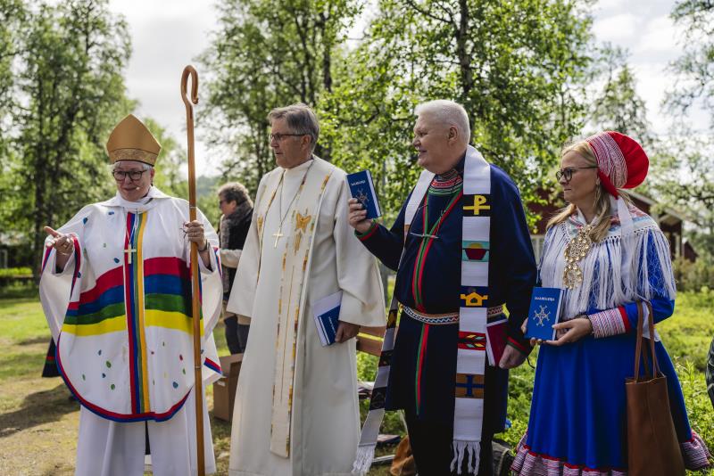 Biskop Eva Nordung-Byström och biskop emeritus Tor Singsaas står utomhus bredvid två personer i samiska kläder.