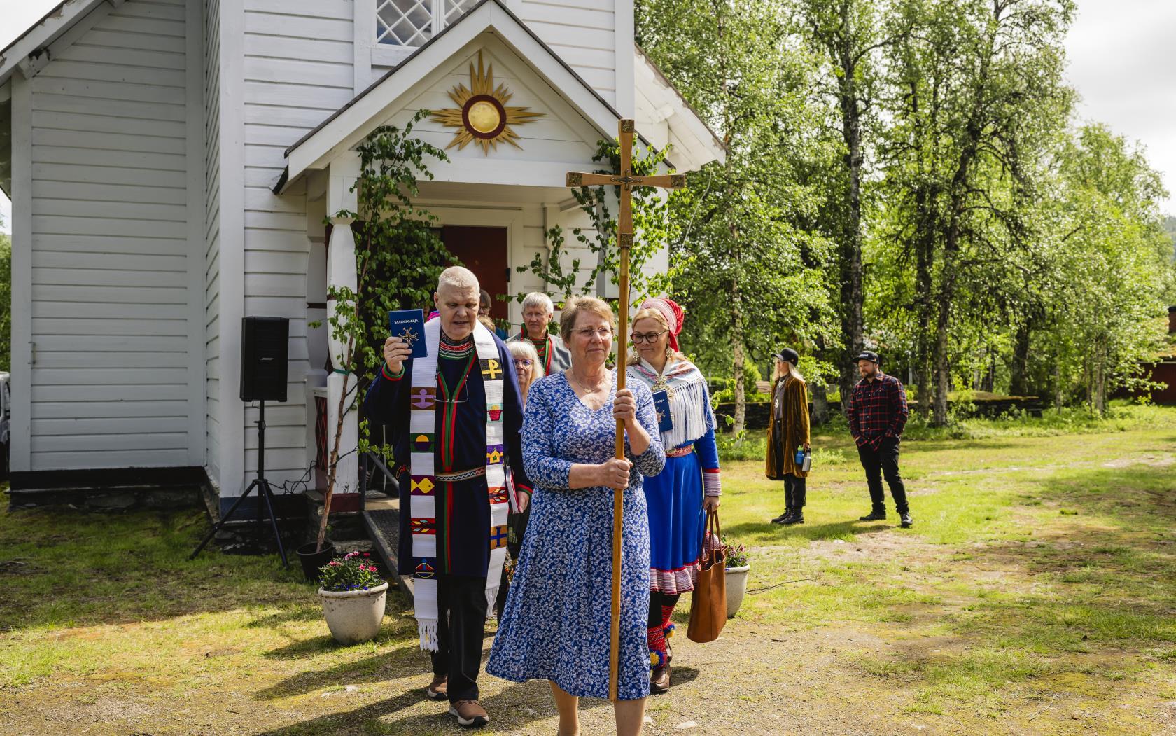 En procession kommer ut ur en liten vit träkyrka.