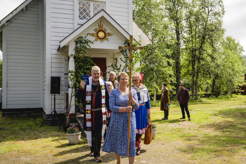 En procession kommer ut ur en liten vit träkyrka.