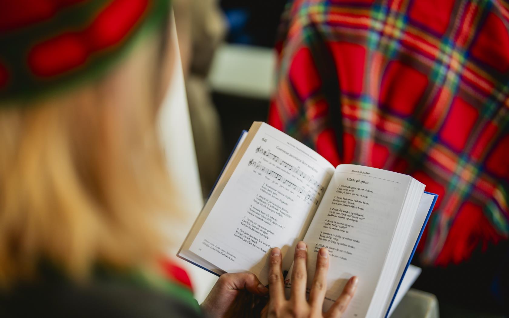 En kvinna i en kyrkbänk har en uppslagen psalmbok i knät.