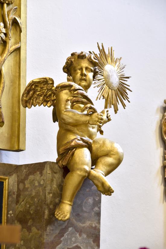 En guldfärgad staty av en ängel sitter på en predikstol i en kyrka.