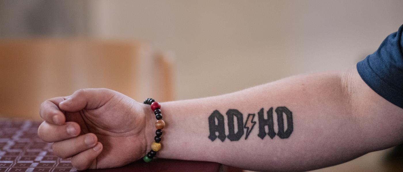 Närbild på någon som tatuerat in ADHD och en blixt på underarmen, likt rockgruppen ACDC.