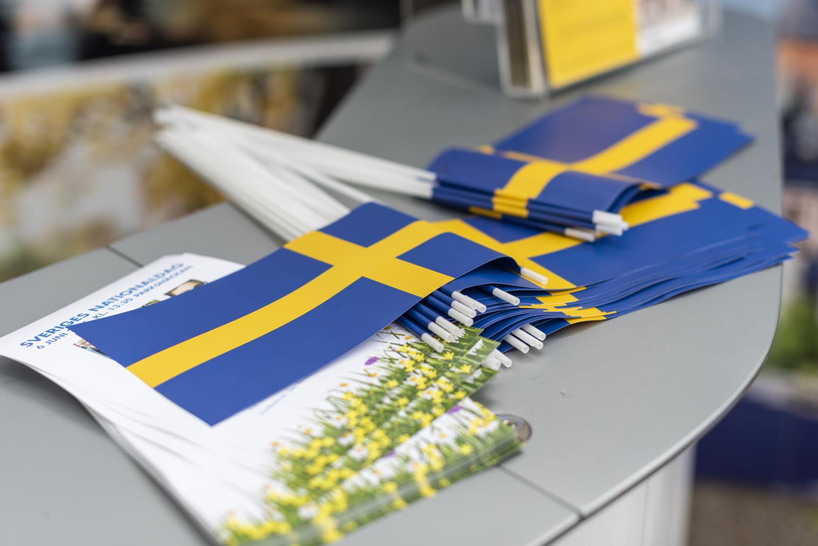 En hög med svenska flaggor och tryckta blad med texten Sveriges nationaldag ligger på en bänkyta.