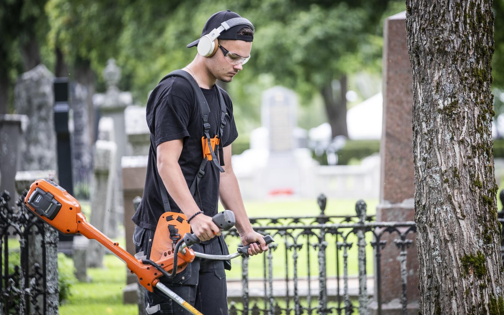 En ung kille klipper gräset med en trimmer på en kyrkogård.