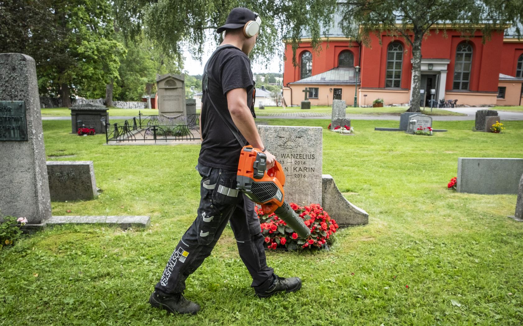 En ung kille går med en lövblås runt bland gravstenarna på en kyrkogård.