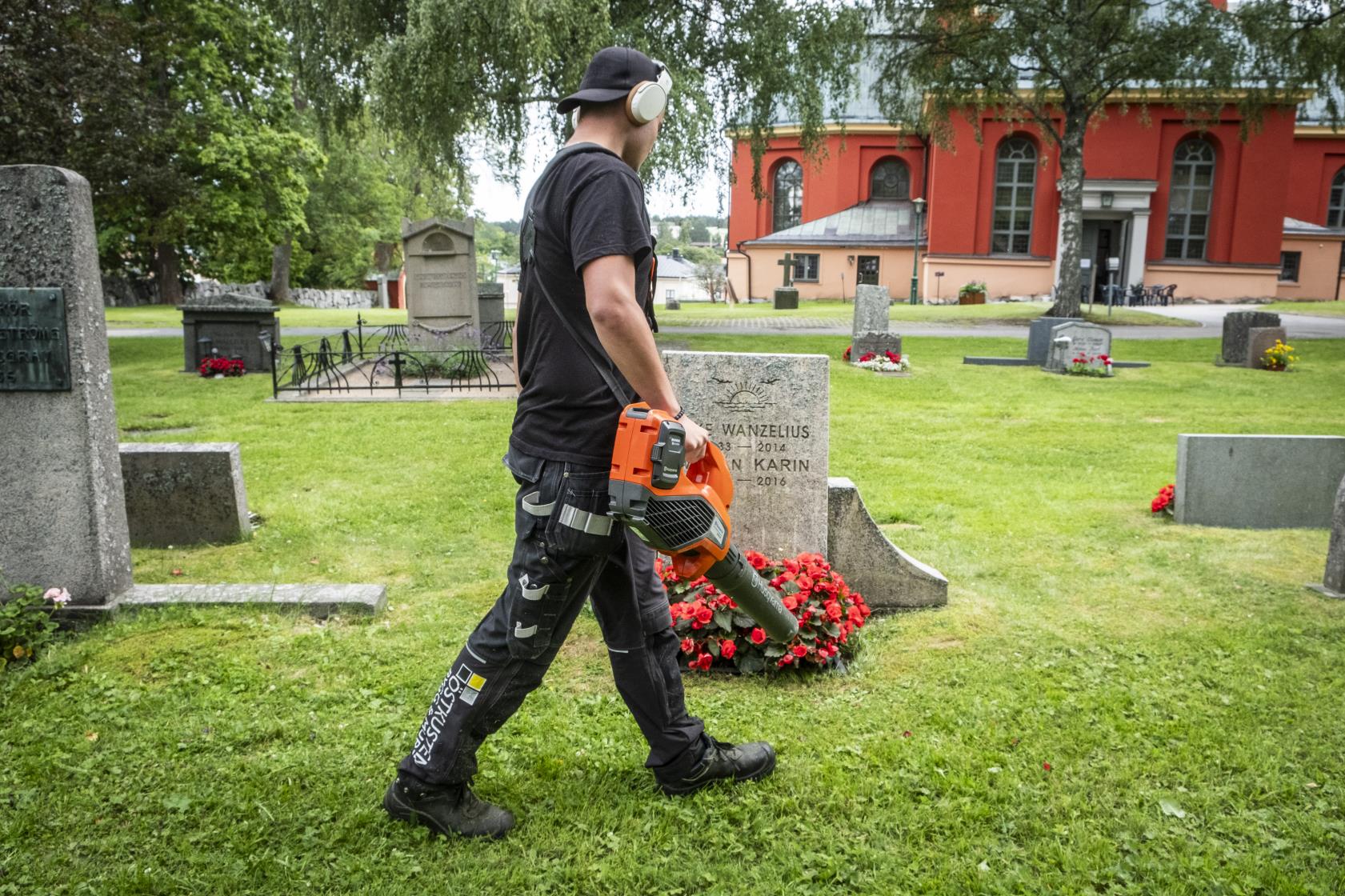 En ung kille går med en lövblås runt bland gravstenarna på en kyrkogård.