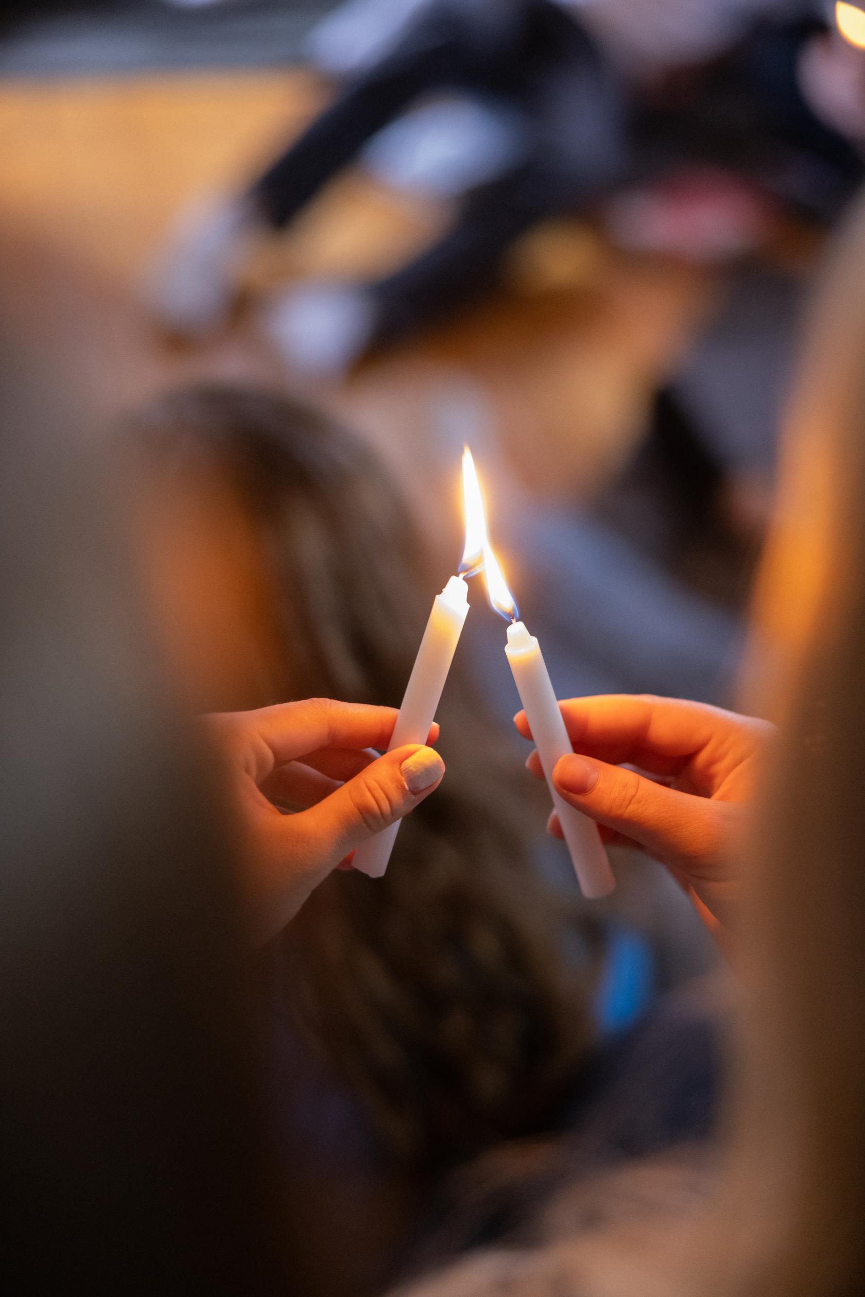 Två personer håller i varsitt stearinljus. Den ena tänder sitt ljus med hjälp av det andra ljusets låga.