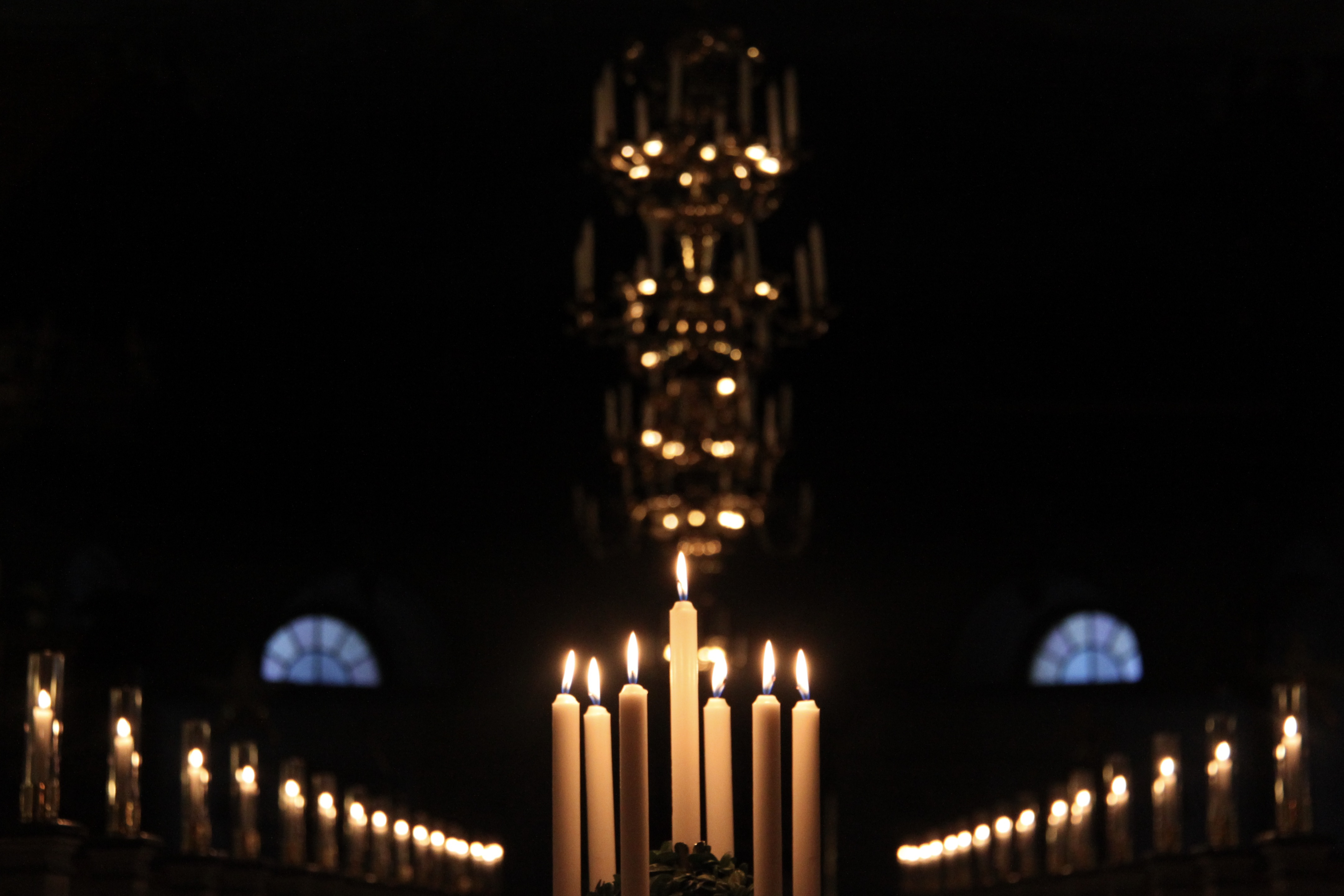 En luciakrona med brinnande ljus i en mörk kyrka.