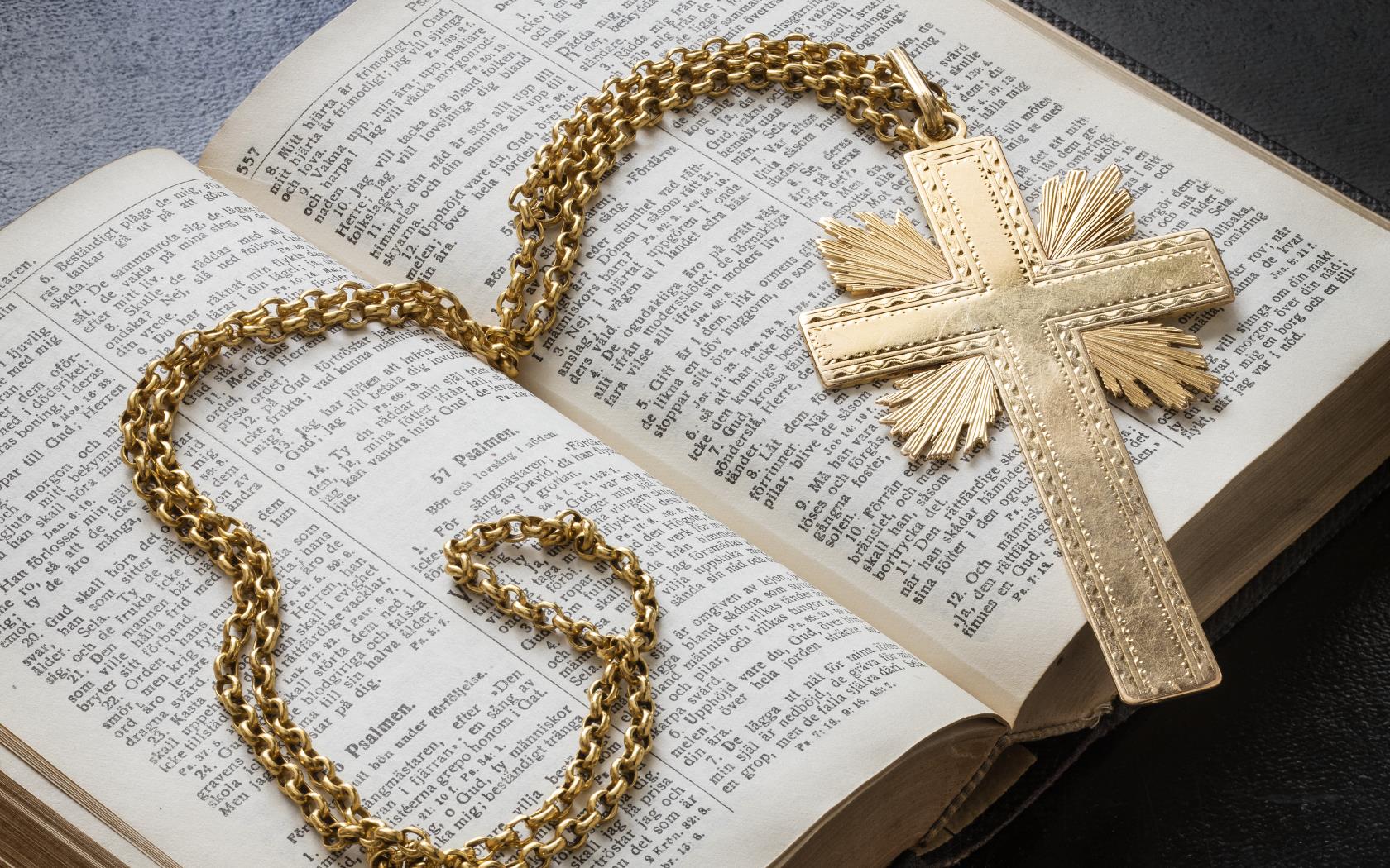 Ett halsband med ett kors av guld ligger i en uppslagen bibel.