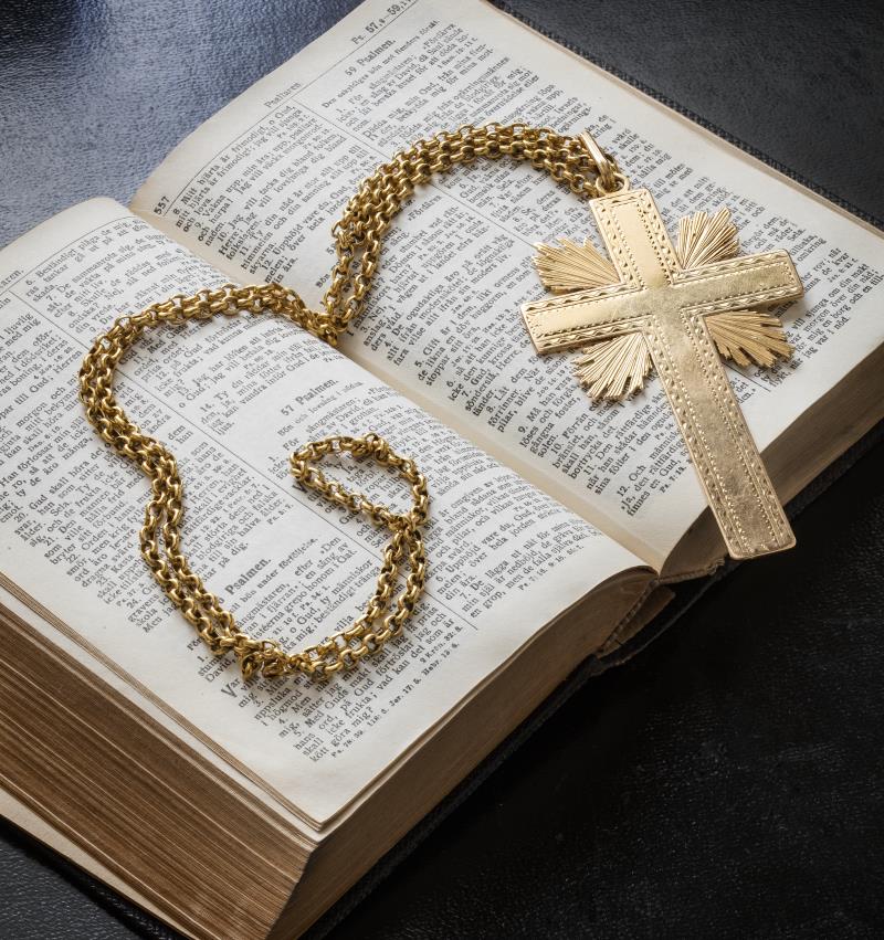 Ett halsband med ett kors av guld ligger i en uppslagen bibel.