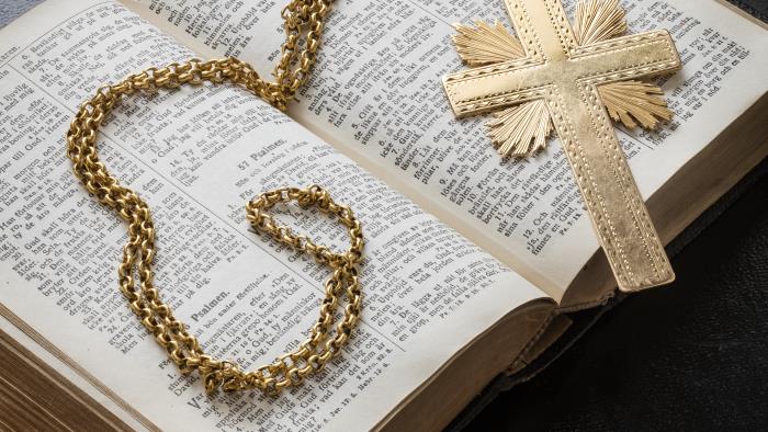 Ett halsband med ett kors av guld ligger i en uppslagen bibel.