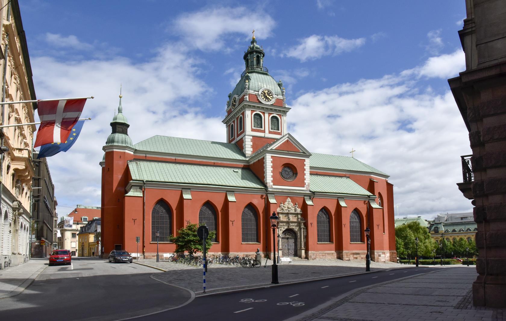 En rödputsad kyrka med grönt koppartak i stadsmiljö.