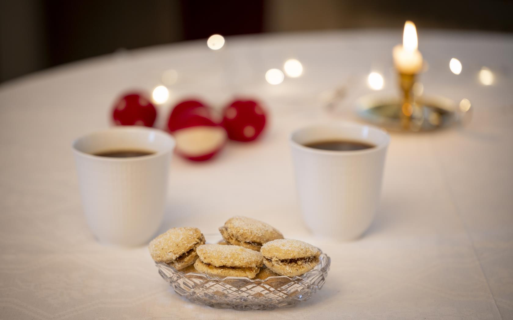 Ett kakfat, två kaffemuggar och ett tänt ljus står på ett bord.