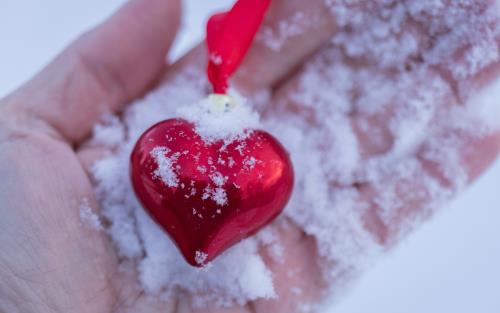 Ett snöigt rött hjärta med siden band ligger i en handflata.