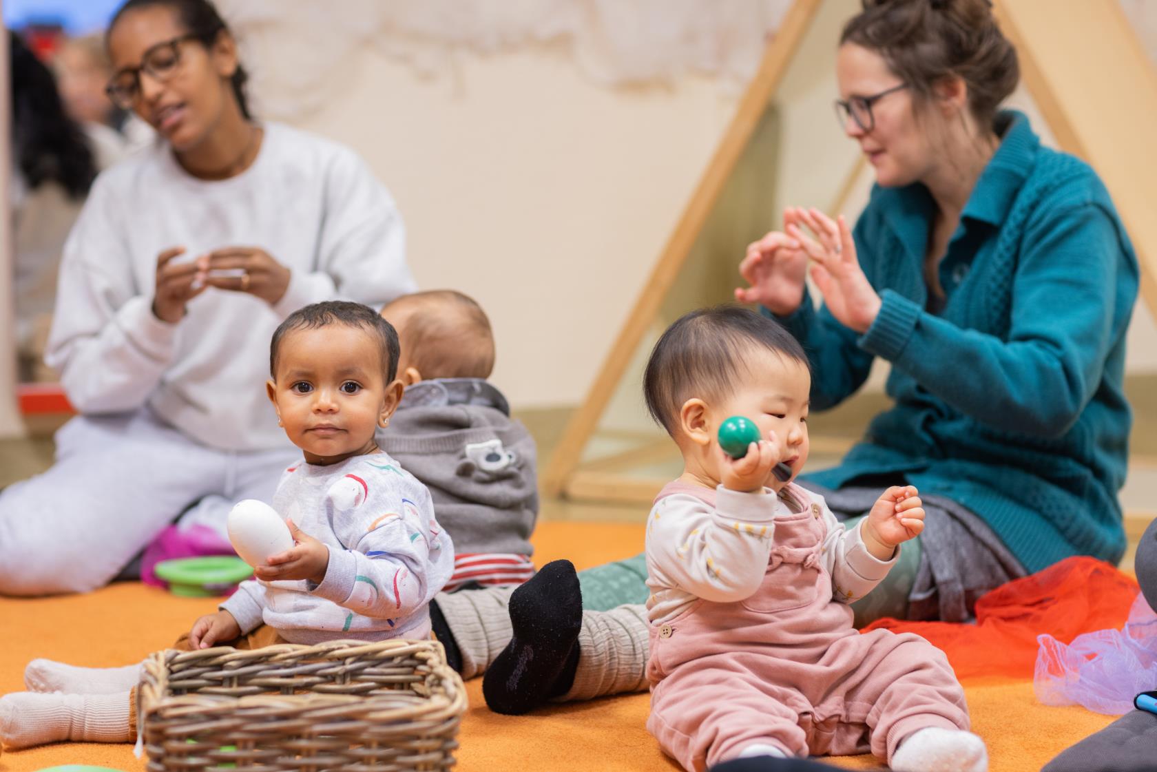 Tre bebisar sitter på golvet. Runt om sitter deras mammor och sjunger.