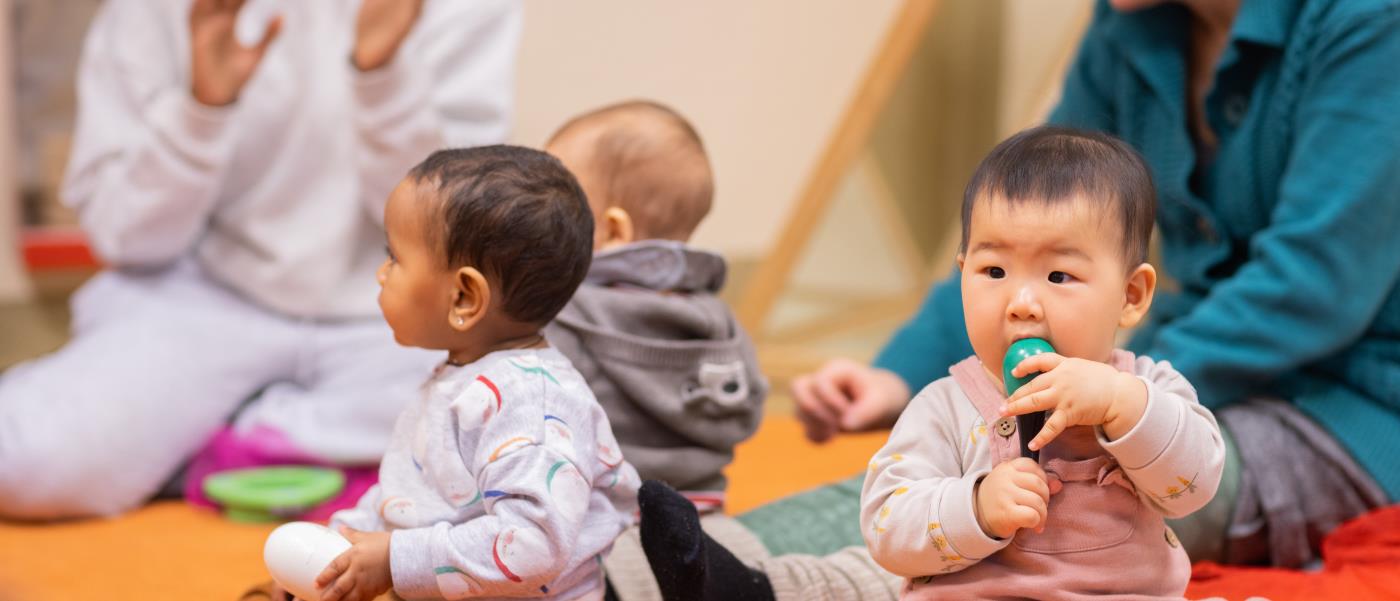 Tre bebisar sitter på en matta. Deras föräldrar sitter runt om.