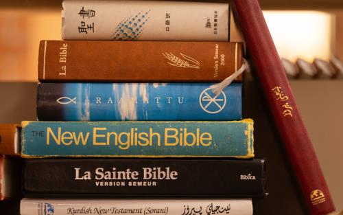 En hög med vältummade biblar på olika språk ligger på ett bord.