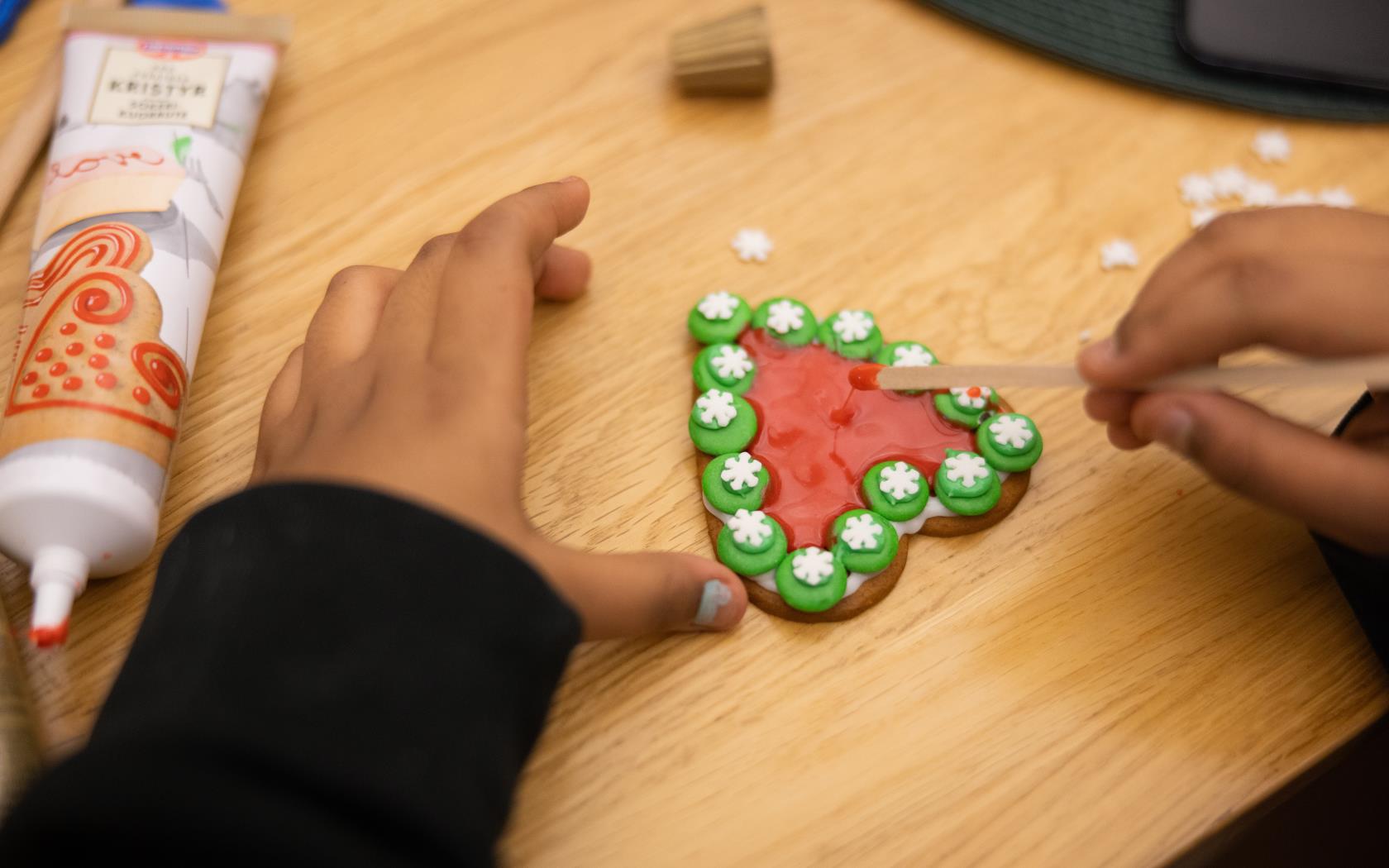 Närbild på ett barns händer som lagt non stop och kristyr på ett pepparkakshjärta.