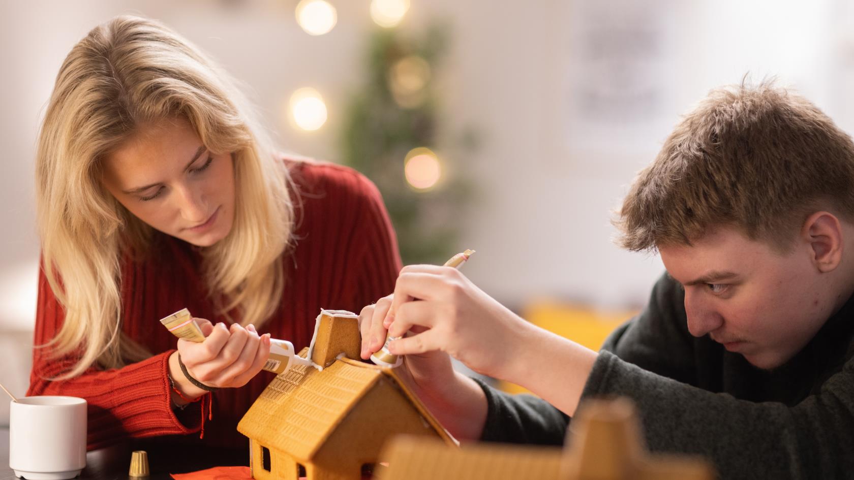 En tjej och en kille i tonåren spritsar ett pepparkakshus.