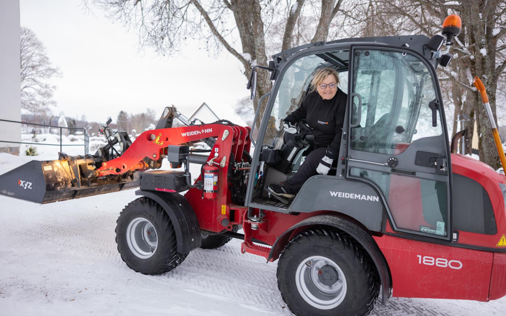 En kvinnlig vaktmästare plogar snö med en liten traktor på kyrkogården.