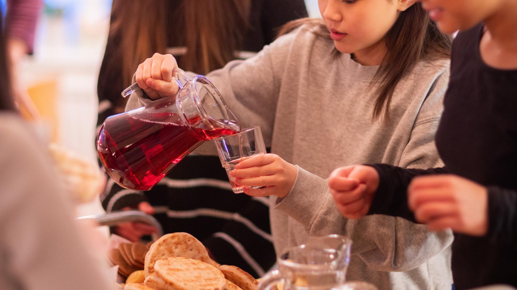 En flicka vid en fikavagn häller upp saft i ett glas. Andra flickor står bredvid.