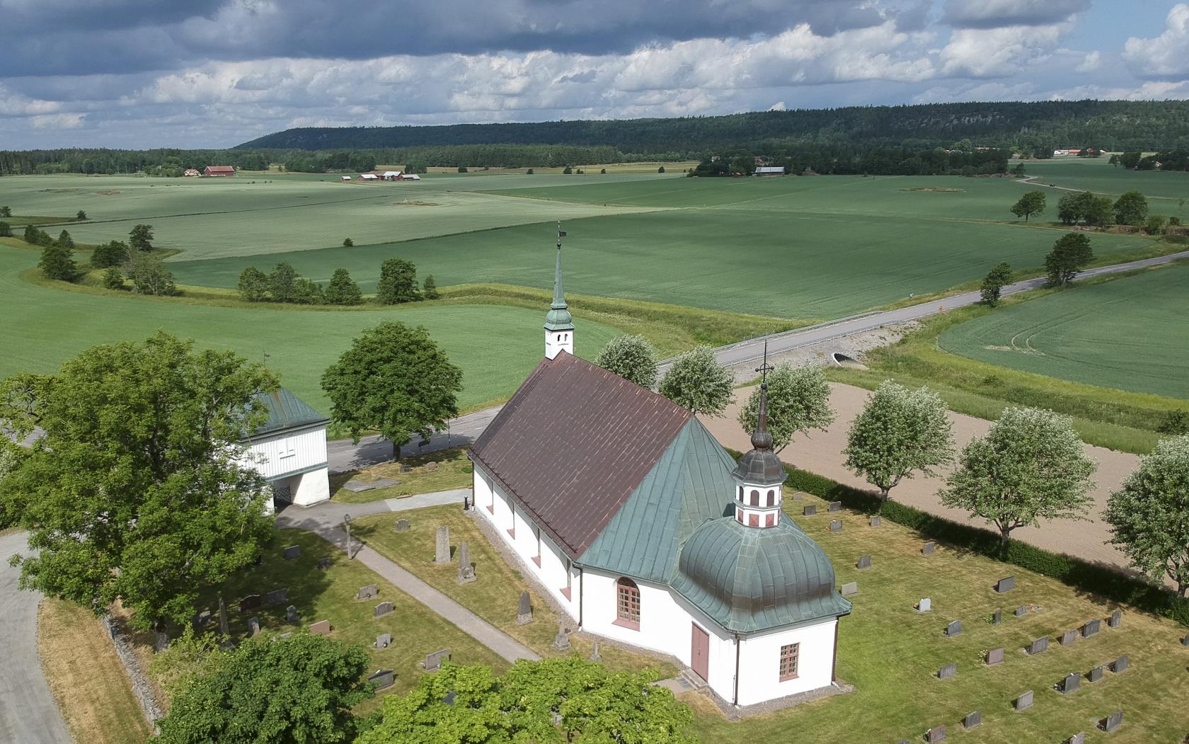 Flygfoto vit kyrka i landsbygd, sommar. 