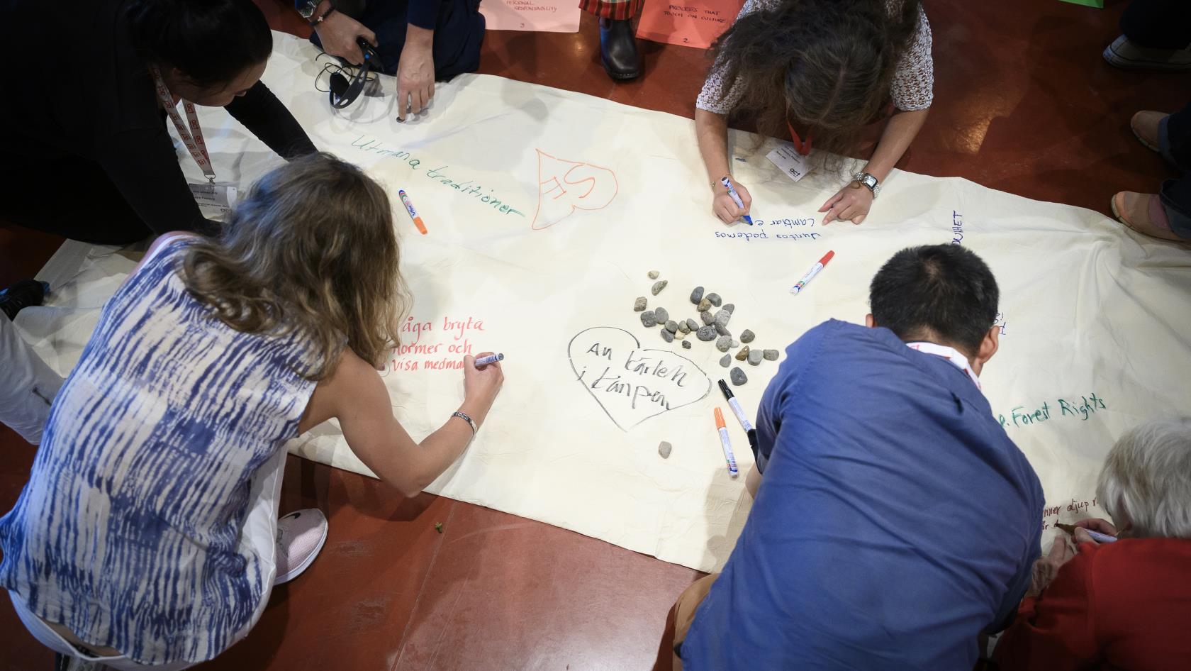 Workshop. Några personer skriver på en stor duk på golvet.