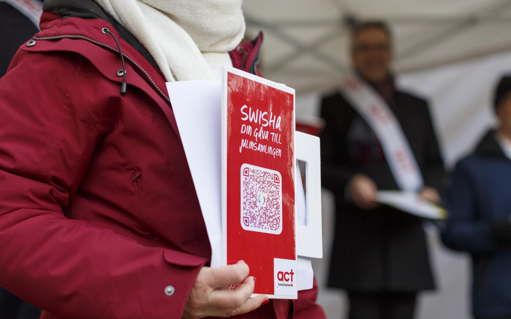 En person håller upp en skylt med texten Swisha din gåva till julinsamlingen.