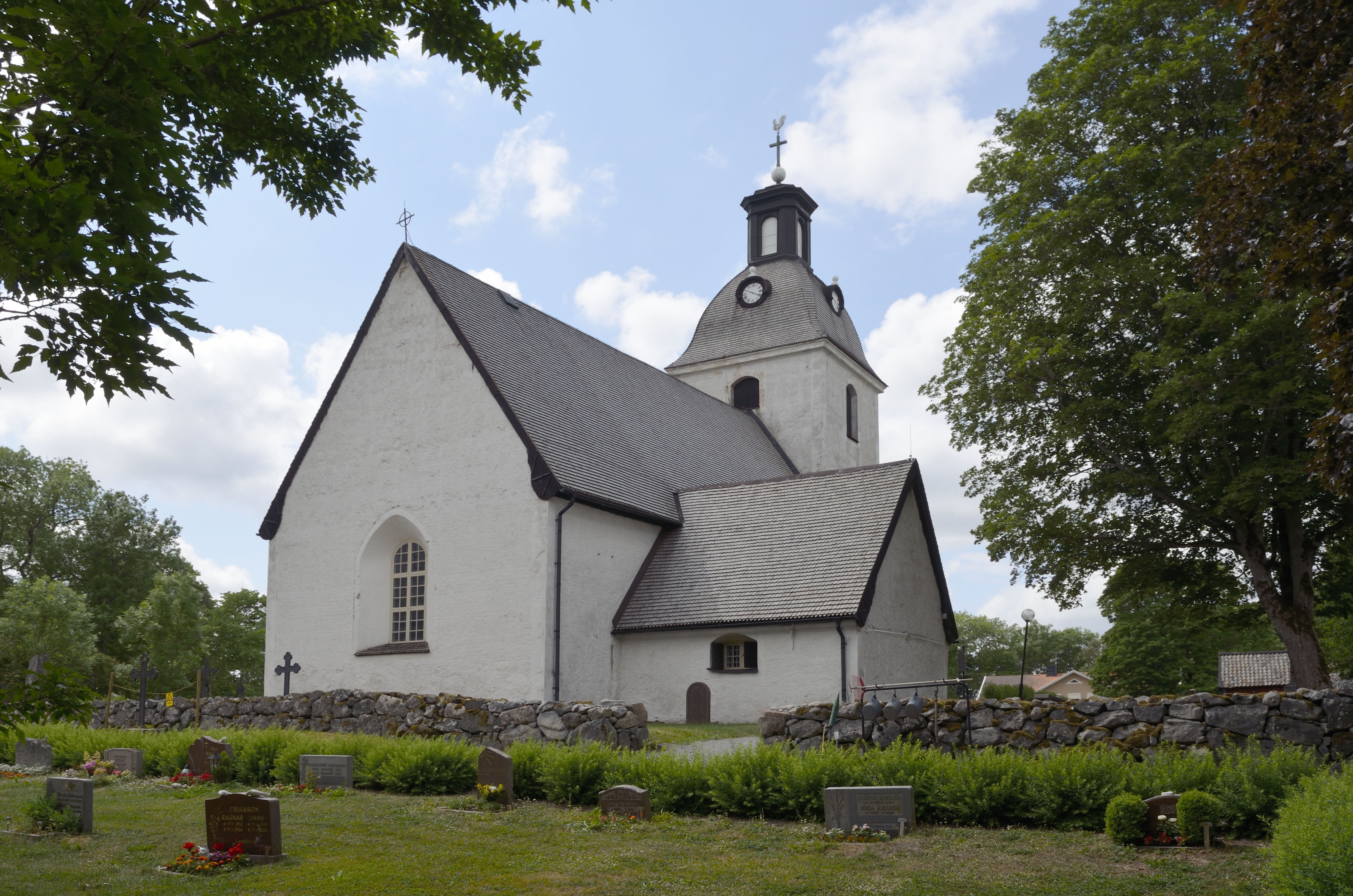 En vit stenkyrka med ett torn, omgiven av gröna träd.